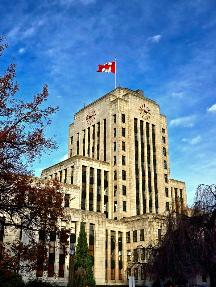 Vancouver City Hall's iconic Art Deco architecture under a bright blue sky, featuring a Canadian flag.